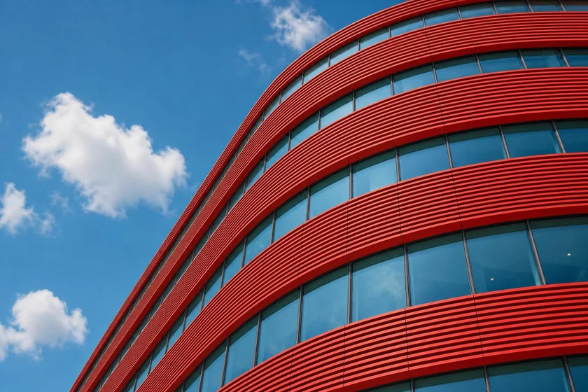 A modern red-clad office building rising against a clear blue sky